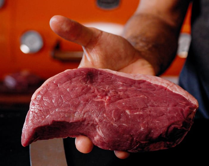 Açougueiro segurando uma picanha inteira com a capa de gordura voltada para cima